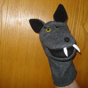 May include: Gray felt hand puppet with a black nose, yellow eyes, and white teeth. The puppet is shaped like a wolf or dog.
