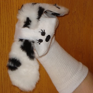 May include: A white sock puppet with a black and white dalmatian fur head and black paw prints on the face.