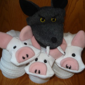 May include: A gray wolf puppet with yellow eyes and a black nose, surrounded by four white pig puppets with pink snouts and black eyes.