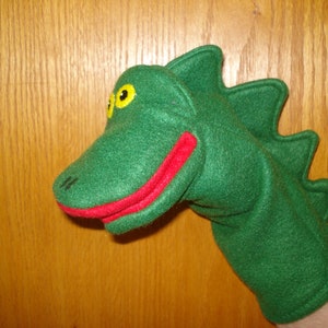 May include: Green felt hand puppet shaped like an alligator with a red mouth and yellow eyes.