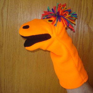 May include: Orange hand puppet with a black mouth and a colorful, spiky hair tuft.