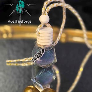 May include: A small, clear, geometric-shaped bottle filled with iridescent blue and purple glitter. It has a wooden cap and a decorative charm. A cream-colored cord with gold accents is attached for hanging.