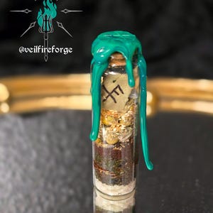 May include: A small glass vial filled with layers of herbs, sand, and other materials, sealed with a cork and topped with bright green wax. The vial contains a small piece of paper with a symbol on it. The vial is reflected in the surface below.