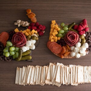 May include: A charcuterie board shaped like a bunny and a cat, with a variety of meats, cheeses, fruits, and vegetables. The board is surrounded by a pile of crackers.