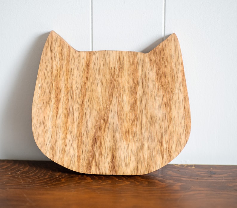 May include: A wooden cat-shaped cutting board with a natural wood grain finish.