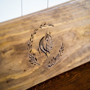 May include: A wooden serving tray with a carved horse head design in a wreath of leaves. The tray has a black metal handle.