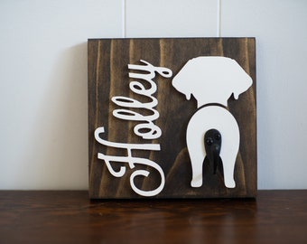 May include: A wooden sign with the name "Holley" written in white cursive lettering. A white silhouette of a dog's rear end is on the right side of the sign, with a black hook attached to the dog's tail.