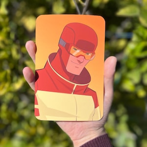 May include: A close-up of a superhero illustration. The character is wearing a red and yellow suit with a red helmet and yellow goggles. The background is a gradient of orange and yellow.
