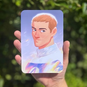 May include: A rectangular art print featuring a portrait of a man with short, light brown hair and blue eyes. He wears a white turtleneck and a design with blue and yellow hues. The background has a soft, blurred effect.