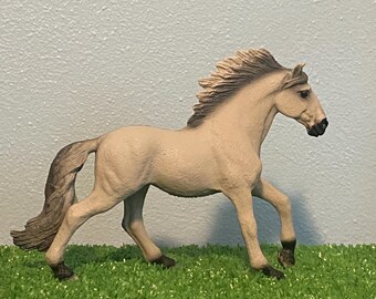 May include: A gray horse figurine with a flowing mane and tail. The horse is standing on a green grassy surface.