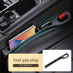 May include: Black seat gap plug for the main driver's side. The plug has a slot for a phone, a key fob, and a red button. The plug is designed to fit in the gap between the car seat and the center console. The text "Seat gap plug" is visible.