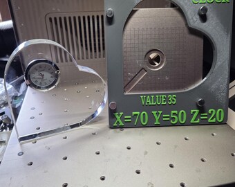 Könnte beinhalten: Eine herzförmige Uhr aus klarem Acryl mit silbernem Zifferblatt und ein grauer rechteckiger Rahmen mit dem grünen Text XTOOL HEART CLOCK, VALUE 35, und X=70 Y=50 Z=20. Der Rahmen enthält einen metallischen, herzförmigen Einsatz mit einem Gitter.