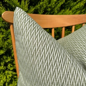 May include: A green and white patterned cushion with a herringbone design. The cushion is sitting on a wooden chair.