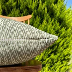 May include: A green and white patterned throw pillow with a zipper closure. The pillow is sitting on a wooden chair.