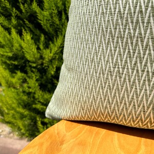 May include: A green and white patterned throw pillow with a chevron design. The pillow is sitting on a wooden surface.