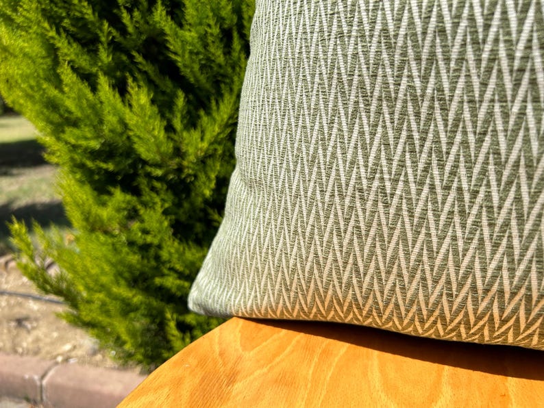 May include: A green and white patterned throw pillow with a chevron design. The pillow is sitting on a wooden surface.