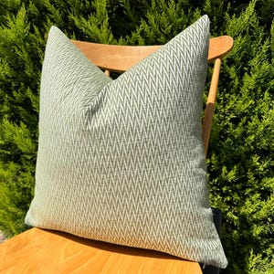 May include: A green and white chevron patterned throw pillow on a wooden chair. The pillow is made of a soft, textured fabric.