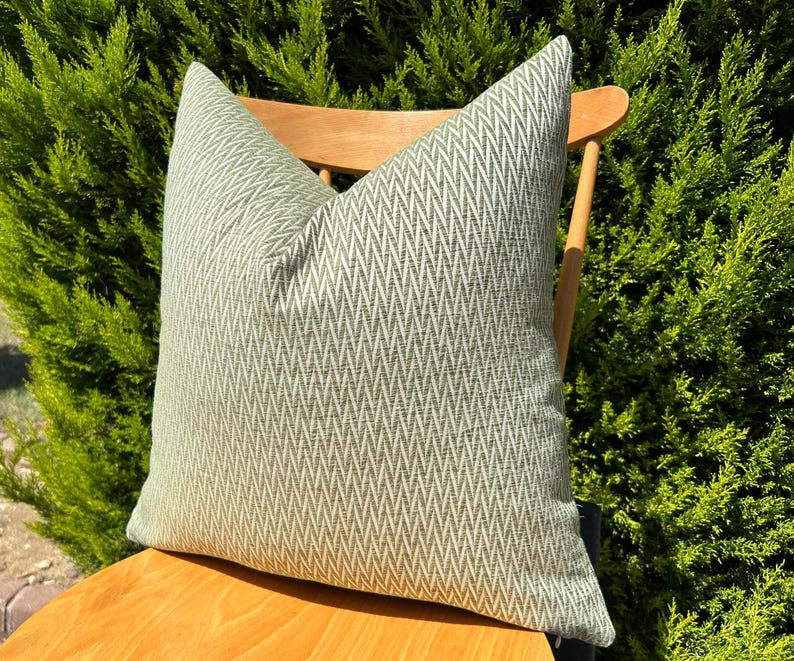 May include: A green and white chevron patterned throw pillow on a wooden chair. The pillow is made of a soft, textured fabric.