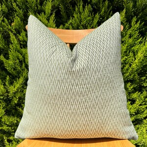 May include: A green and white patterned throw pillow with a chevron design. The pillow is sitting on a wooden chair.