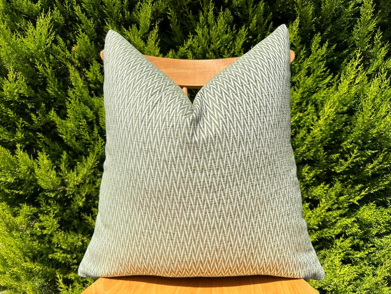 May include: A green and white patterned throw pillow with a chevron design. The pillow is sitting on a wooden chair.