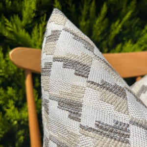 Peut inclure: Gros plan sur un coussin de canapé blanc et gris à motifs géométriques. Le coussin est sur une chaise en bois.