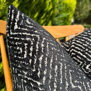May include: Two black and white patterned throw pillows on a wooden chair. The pillows have a geometric design with white lines on a black background.