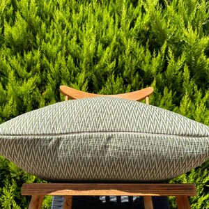 May include: A green and white chevron patterned throw pillow on a wooden chair. The pillow is made of a soft, textured fabric.