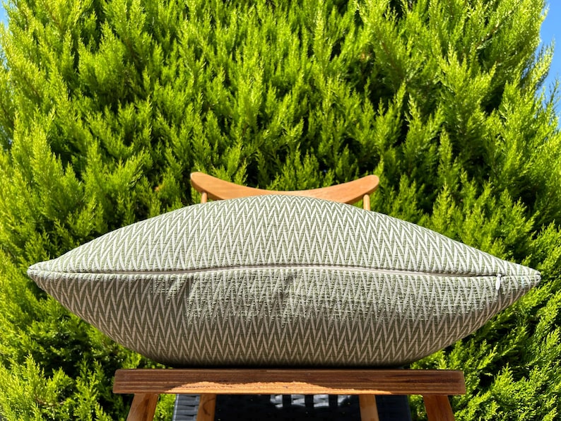 May include: A green and white chevron patterned throw pillow on a wooden chair. The pillow is made of a soft, textured fabric.