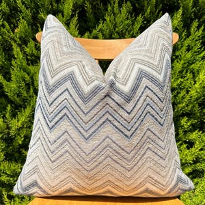May include: A decorative throw pillow with a chevron pattern in shades of gray and blue.