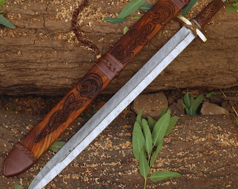 May include: A handcrafted sword with a patterned steel blade and a wooden handle. The sword rests beside its wooden sheath, which features intricate carved designs and leather accents. The overall color scheme is brown and silver.