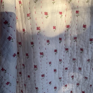May include: White cotton quilt with a repeating pattern of small pink flowers. The quilt is quilted with a thin red thread.