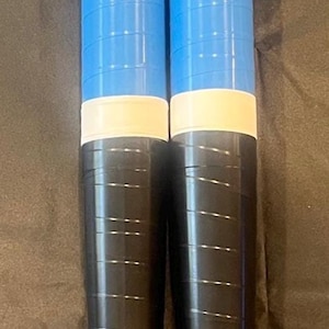 May include: Two cylindrical objects, likely sports equipment, are shown. They are primarily blue and black, with a white band and a cartoon character on the top. The bottom has blue and black stripes.