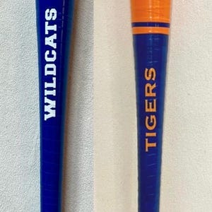 May include: Two baseball bats, one blue with "WILDCATS" and a team logo, the other orange with "TIGERS" and a team logo. The bats have blue and white grips.
