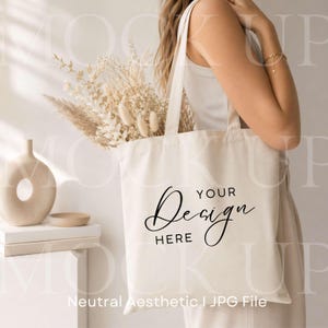 Könnte beinhalten: Cremefarbene Tragetasche mit den Worten "YOUR Design HERE" in eleganter Schrift. Die Tasche ist mit Trockenblumen gefüllt und wird von einer Person gehalten. Das Bild hat eine neutrale Ästhetik.