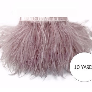 May include: A strip of mauve ostrich feathers with a satin ribbon backing. The feathers are dense and soft, creating a fluffy texture. The image includes a white circle with the text "10 yards".