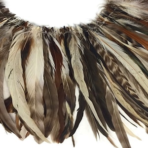 Puede incluir: Una larga hebra de plumas marrones, beige y blancas. Las plumas están dispuestas en cascada, creando una franja decorativa.