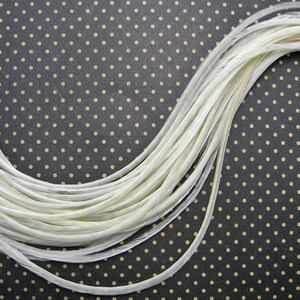 May include: A bundle of white feathers arranged in a curved shape on a black background with white polka dots.