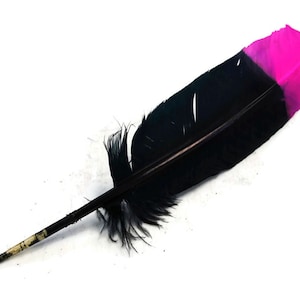 Puede incluir: Una pluma negra con una punta rosa. La pluma está sobre una superficie blanca.