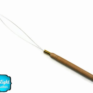 Puede incluir: Un enhebrador de agujas de madera con una punta de metal dorado y una aguja de metal fina y curva. El enhebrador de agujas está diseñado para ayudar a enhebrar las agujas fácilmente.