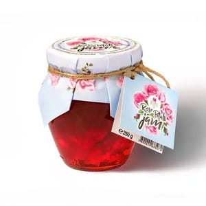 Peut inclure: Un pot en verre rempli de confiture de pétales de rose rouge vif. Le couvercle est recouvert d'un papier blanc orné d'illustrations de roses roses, fixé par une ficelle brune. Une étiquette carrée attachée à la ficelle indique Rose Petals jam 250 g.