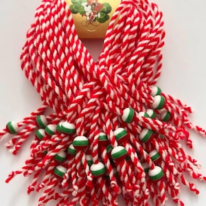May include: Red and white braided yarn bracelets with green and white beads. The bracelets are tied together and have a small yellow tag with a graphic of a ladybug and shamrocks.