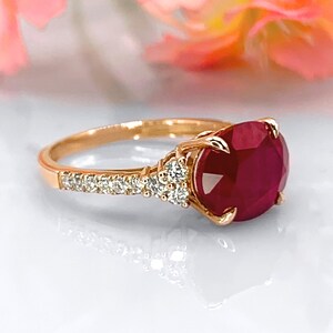Può includere: Anello in oro rosa con una grande gemma di rubino rosso scuro rotonda. La fascia è decorata con piccole pietre chiare. Un gioiello classico ed elegante.