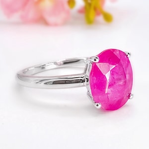Puede incluir: Un anillo de plata con una gran gema rosa brillante de corte ovalado. La gema está engastada en un engaste clásico de cuatro puntas. La banda del anillo es de plata pulida, creando un contraste llamativo con la gema brillante.