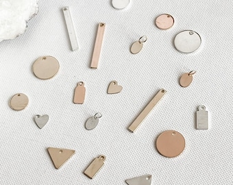 May include: Assortment of metal charms in various shapes and sizes, including circles, hearts, triangles, and rectangles. The charms are made of silver, gold, and rose gold.