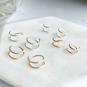 May include: A close-up of a white plate with six pairs of small, silver and gold hoop earrings. The earrings are arranged in a circular pattern.