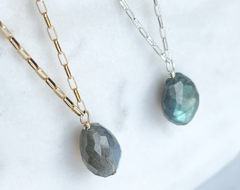 May include: Two delicate necklaces with a teardrop-shaped labradorite gemstone pendant. One necklace has a gold chain and the other has a silver chain.