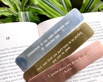May include: Four metal bookmarks with different quotes engraved on them. The quotes are: "Literature is the most agreeable way of ignoring life", "And now that you don't have to be perfect, you can be good.", "I guess there are never enough books", and "Remarkable is the most agreeable way of ignoring life".