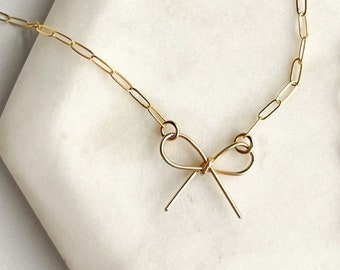May include: A gold chain necklace with a delicate gold bow pendant.