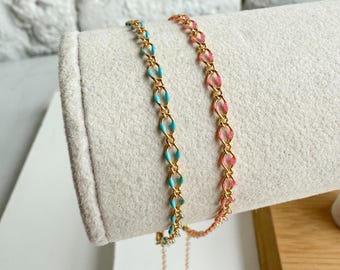 May include: Two delicate gold chain bracelets. One bracelet features turquoise enamel links, the other has pink enamel links. Both bracelets are displayed on a light gray surface, showcasing their intricate design and color contrast.