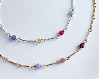 May include: Two delicate necklaces with silver and gold chains, featuring colorful gemstone beads. The top necklace has purple, yellow, and red beads, while the bottom necklace has purple, pink, and red beads.
